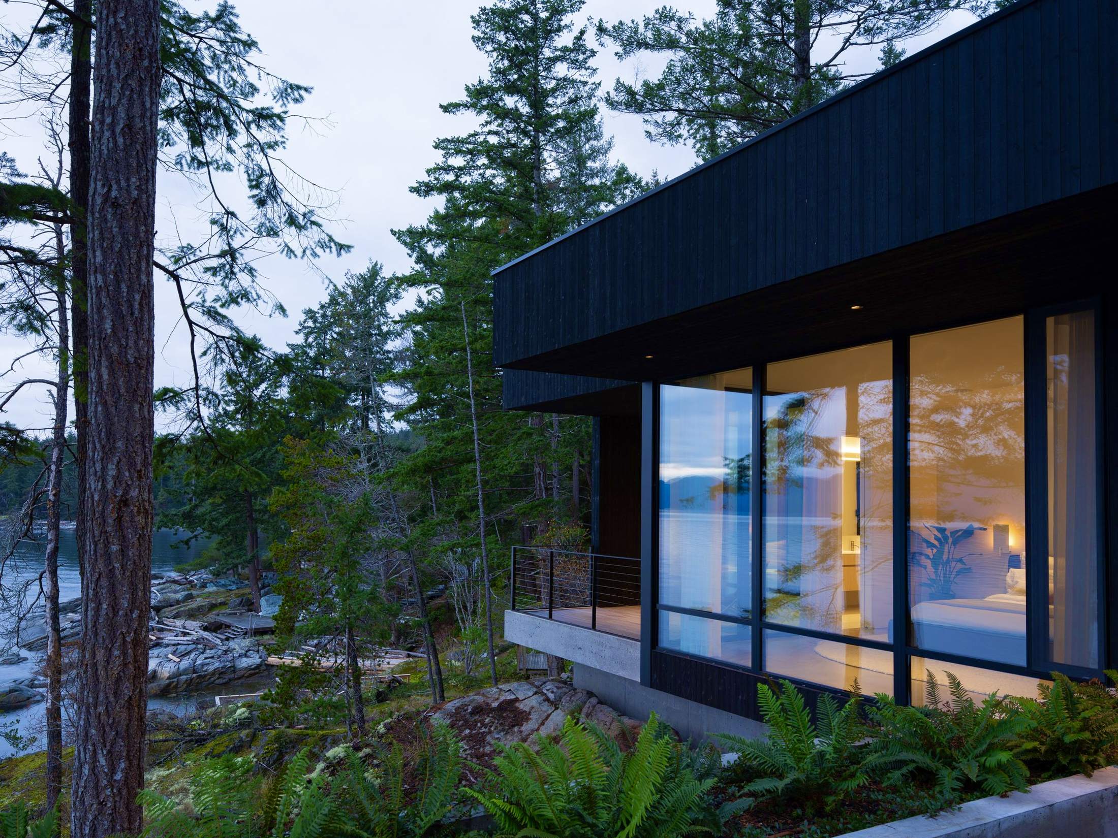 West coast home at dusk on a rocky Sunshine Coast shoreline, framed by firs and ferns