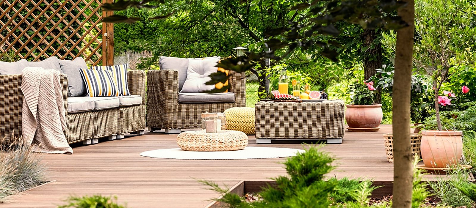 Landscaped garden deck with wicker seating, potted shrubs and flowering plants